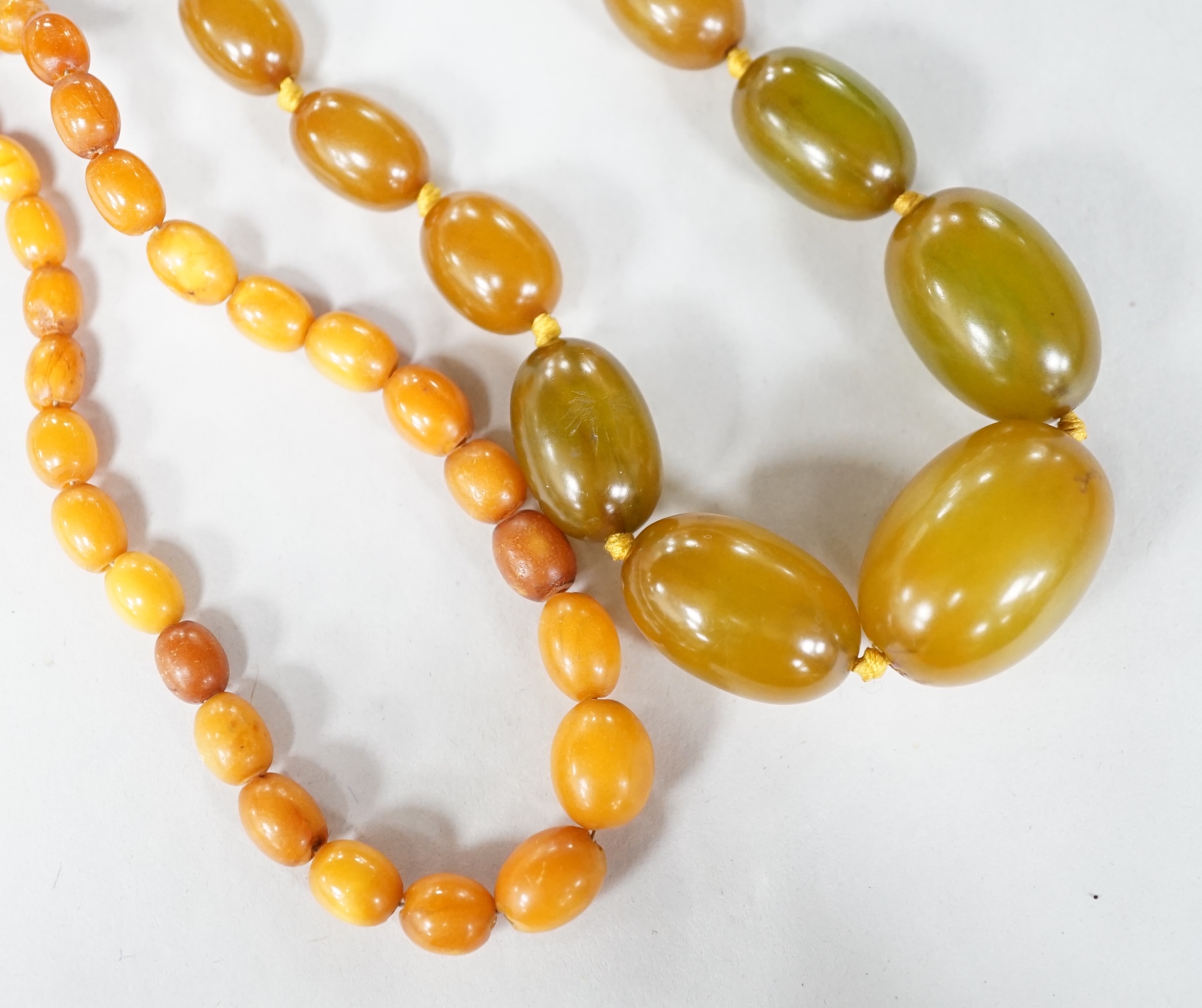 A small single strand graduated oval amber bead necklace, 40cm, gross weight 13 grams, together with a single strand graduated simulated green amber oval bead necklace, 54cm, gross weight 55 grams. Condition - poor to fa